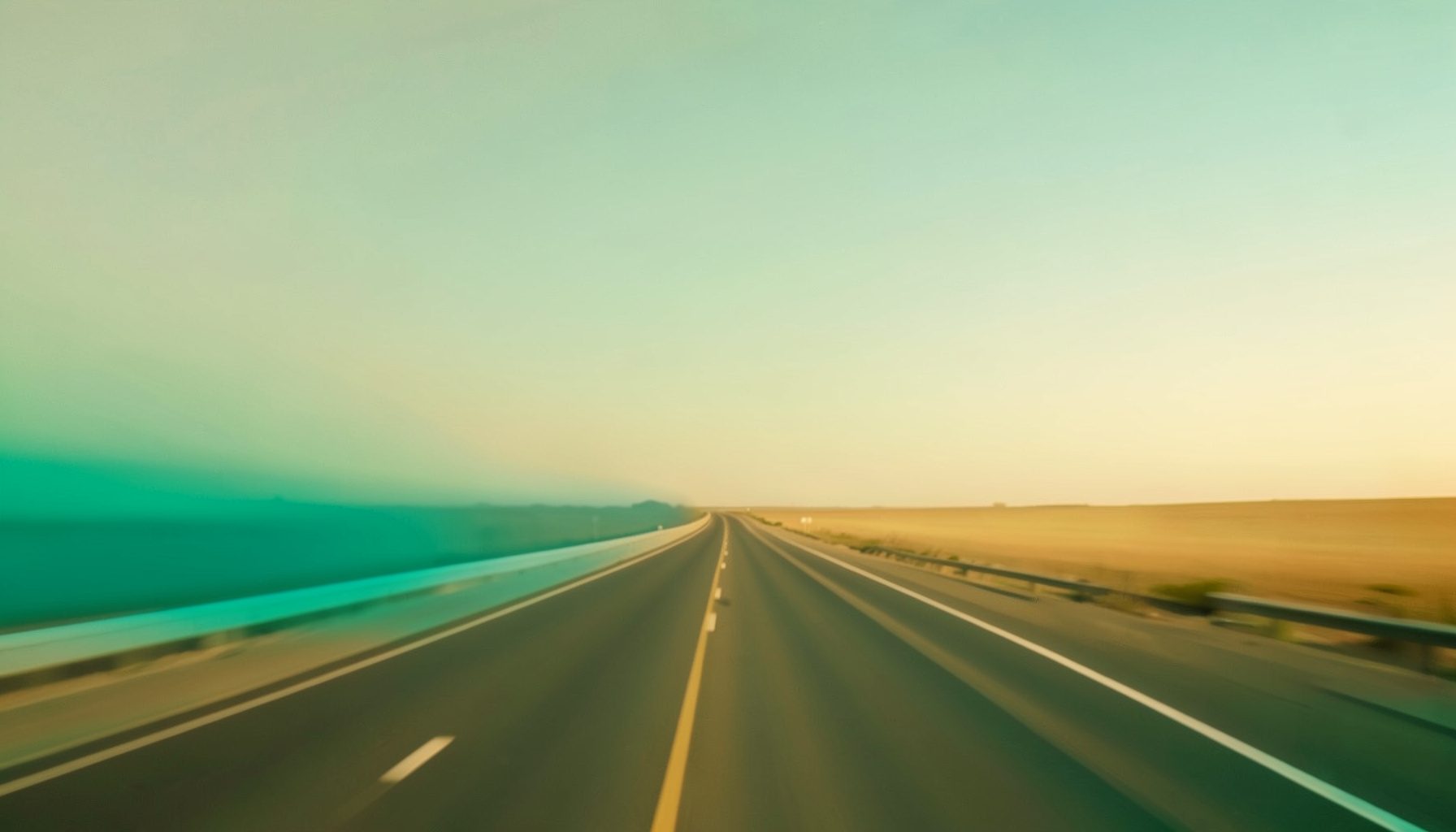 Warm-toned photograph of a highway stretching toward the horizon under a broad sky, with soft golden light and muted earth tones